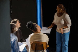 Group drama therapy session with participants role-playing and reading scripts to explore healing through creative expression.
